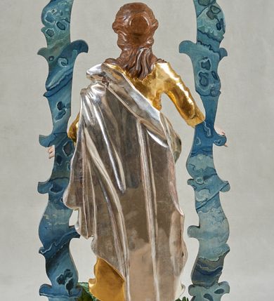 Zdjęcie nr 2: Postawa na planie prostokąta, obwiedziona profilowanym gzymsem, z otworami na drążki. Na niej ustawiona pełnoplastyczna figura Marii stojącej na globie oplecionym przez węża. Matka Boska ukazana frontalnie, z rękami rozłożonymi na boki, lewą stopą depcze głowę węża. Twarz ma owalną, o wysokim czole, wąskich oczach skierowanych w górę, krótkim nosie i wąskich ustach; okoloną długimi, brązowymi włosami, częściowo upiętymi z tyłu, a częściowo opadającymi na ramiona i kark. Ubrana jest w złoconą suknię, przepasaną w talii oraz srebrzony płaszcz przewiązany diagonalnie przez lewe ramię i opadający na plecy oraz prawą nogę. Polichromia ciała naturalistyczna. Nad figurą uproszczony czerwony baldachim z żółtym lambrekinem, wsparty na fantazyjnie wyciętych listewkach, polichromowanych razem z podstawą na sposób imitujący marmoryzację w kolorze niebiesko-szarym. 