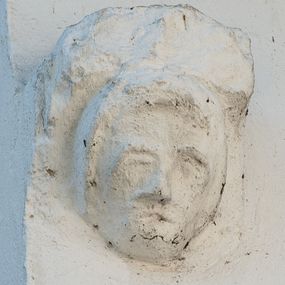 Zdjęcie nr 1: Wspornik w formie męskiej, owalnej twarzy, podtrzymującej półkolistą płytę. Twarz o zaznaczonych umownie oczodołach i łukach brwiowych, z wyodrębnionym krótkim nosem i szczeliną w miejscu ust; okolona krótkimi włosami, z grzywką nad czołem.



