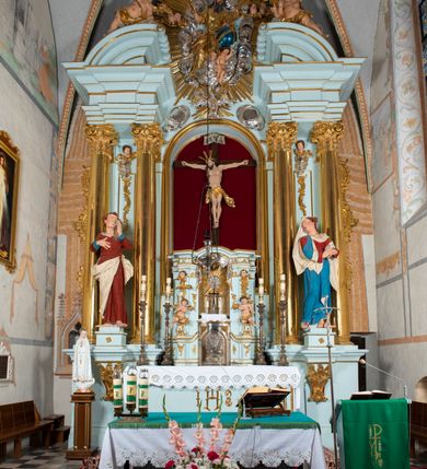 Zdjęcie nr 4: Tabernakulum pancerne, w formie drewnianej, prostopadłościennej skrzynki obitej blachą, o wypukłej ściance frontowej. Drzwiczki w formie kwadratu zamkniętego łukiem półkolistym, ujęte wzorzystym pasem, z trybowanym przedstawieniem baranka z krzyżem, leżącego na księdze, w glorii promienistej. W górnych narożach ścianki frontowej aplikowane elementy ornamentalne. Tabernakulum w drewnianej, architektonicznej obudowie, wpisane w cokół, na którym znajduje się tron wystawienia. Tron w formie niszy, ujęty dwiema parami zdwojonych pilastrów. Wewnętrza para wysunięta jest do przodu, a jej trzony dekorowane rocaille'm, kłosami zbóż, winogronami oraz główkami anielskimi przechodzą w spływy wolutowe, na których klęczą aniołki. Pilastry dźwigają belkowanie, wyłamane na ich osi, częściowo przerwane nad niszą środkową, z wyłamanym odcinkowo gzymsem, z podwieszoną tkaniną. Pilastry zewnętrzne ujęte wolutami spływającymi na wyłamane partie cokołu. Podstawa, pilastry i fryz dekorowane rocaille'm. Struktura polichromowana w kolorze błękitnym, ze złoconymi profilami i ornamentyką, tkanina srebrzona. 