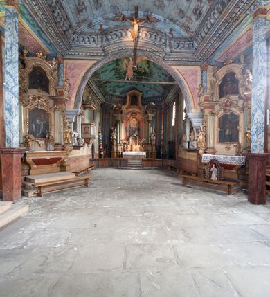 Zdjęcie nr 9: Kościół drewniany o konstrukcji zrębowej, elewacje jednolite, szalowane gontem. Wieża oraz kruchty zachodnia i południowa o konstrukcji słupowo-ramowej, kruchty szalowane deskami. Więźba dachowa drewniana, krokwiowa. Budynek na kamiennym podmurowaniu. 
Kościół orientowany, jednonawowy, nawa na rzucie prostokąta, prezbiterium węższe, wydłużone, zakończone trójbocznie. Do północnej ściany prezbiterium przylega zakrystia o wschodniej ścianie skośnej, będącej przedłużeniem bocznej ściany apsydy. 
Przy zachodniej ścianie nawy wieża na planie zbliżonym do kwadratu o wtórnym podziale na sale wystawiennicze (w przyziemiu wieży muzeum). Przy nawie od południa i przy wieży od frontu kruchty na planie kwadratu. 
Pomiędzy nawą a prezbiterium otwór tęczowy. 
Wnętrze nawy i prezbiterium nakryte pozornym sklepieniem kolebkowym, z zaskrzynieniami w nawie, podpartymi filarami o żłobkowanych trzonach, na cokołach, po trzy z każdej strony. Skrajem zaskrzynień nawy oraz górą ścian prezbiterium biegnie dekoracyjny gzyms drewniany, podparty w węgłach apsydy prezbiterialnej żłobkowanymi pilastrami. Łuk tęczowy półkolisty, wsparty na drewnianych konsolach. Otwory drzwiowe o prostokątnym wykroju zamknięte drzwiami obitymi deskami z metalowymi okuciami z prezbiterium do zakrystii, z nawy do kruchty południowej i z nawy do wieży. Okna w formie stojącego prostokąta zamkniętego łukiem odcinkowym, dwa w południowej ścianie prezbiterium, a w północnej dwa ślepe oraz cztery pary okien w północnej i południowej ścianie nawy. Na zamknięciu prezbiterium okulus z witrażem. Parapet chóru muzycznego w zachodniej części nawy, wsparty na dwóch drewnianych filarach, z wejściem z nawy po drabiniastych schodach z balustradą. Ściany i sklepienia pokryte polichromią z iluzjonistyczną architekturą i scenami figuralnymi. Posadzka kamienna.
Elewacja frontowa jednoosiowa. Na osi wejście do kruchty zachodniej. Korpus wieży o pochyłych ścianach, silnie zwężających się ku górze, zwieńczonych izbicą, ozdobioną u dołu koronką w formie zębów z frędzlami. Ściany kościoła, oprócz zakrystii i krucht szalowanych deskami, osłonięte rzędami gontów i opatrzone u dołu fartuchami. Na elewacji wschodniej ogrójec. 
Dach wyniosły, wspólny dla nawy i prezbiterium, hełm wieży cebulasty z latarnią, a w połowie długości dachu, nad nawą, wbudowana wieżyczka na sygnaturkę, wszystko kryte gontem. Kruchty nakryte osobnymi daszkami hełmowymi, baniastymi, krytymi gontem. 

Wokół kościoła rośnie starodrzew. Plac zamknięty kamiennym murem nakrytym drewnianym daszkiem dwuspadowym z 2 bramami i z 14 wieżyczkami (kapliczki-stacyjki) nakrytymi daszkami drewnianymi czterospadowymi. 