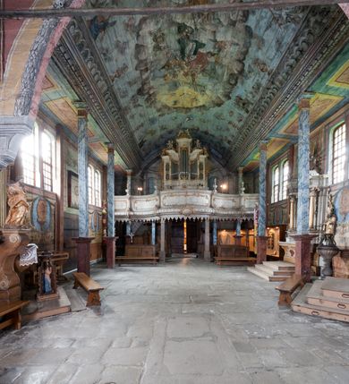 Zdjęcie nr 10: Kościół drewniany o konstrukcji zrębowej, elewacje jednolite, szalowane gontem. Wieża oraz kruchty zachodnia i południowa o konstrukcji słupowo-ramowej, kruchty szalowane deskami. Więźba dachowa drewniana, krokwiowa. Budynek na kamiennym podmurowaniu. 
Kościół orientowany, jednonawowy, nawa na rzucie prostokąta, prezbiterium węższe, wydłużone, zakończone trójbocznie. Do północnej ściany prezbiterium przylega zakrystia o wschodniej ścianie skośnej, będącej przedłużeniem bocznej ściany apsydy. 
Przy zachodniej ścianie nawy wieża na planie zbliżonym do kwadratu o wtórnym podziale na sale wystawiennicze (w przyziemiu wieży muzeum). Przy nawie od południa i przy wieży od frontu kruchty na planie kwadratu. 
Pomiędzy nawą a prezbiterium otwór tęczowy. 
Wnętrze nawy i prezbiterium nakryte pozornym sklepieniem kolebkowym, z zaskrzynieniami w nawie, podpartymi filarami o żłobkowanych trzonach, na cokołach, po trzy z każdej strony. Skrajem zaskrzynień nawy oraz górą ścian prezbiterium biegnie dekoracyjny gzyms drewniany, podparty w węgłach apsydy prezbiterialnej żłobkowanymi pilastrami. Łuk tęczowy półkolisty, wsparty na drewnianych konsolach. Otwory drzwiowe o prostokątnym wykroju zamknięte drzwiami obitymi deskami z metalowymi okuciami z prezbiterium do zakrystii, z nawy do kruchty południowej i z nawy do wieży. Okna w formie stojącego prostokąta zamkniętego łukiem odcinkowym, dwa w południowej ścianie prezbiterium, a w północnej dwa ślepe oraz cztery pary okien w północnej i południowej ścianie nawy. Na zamknięciu prezbiterium okulus z witrażem. Parapet chóru muzycznego w zachodniej części nawy, wsparty na dwóch drewnianych filarach, z wejściem z nawy po drabiniastych schodach z balustradą. Ściany i sklepienia pokryte polichromią z iluzjonistyczną architekturą i scenami figuralnymi. Posadzka kamienna.
Elewacja frontowa jednoosiowa. Na osi wejście do kruchty zachodniej. Korpus wieży o pochyłych ścianach, silnie zwężających się ku górze, zwieńczonych izbicą, ozdobioną u dołu koronką w formie zębów z frędzlami. Ściany kościoła, oprócz zakrystii i krucht szalowanych deskami, osłonięte rzędami gontów i opatrzone u dołu fartuchami. Na elewacji wschodniej ogrójec. 
Dach wyniosły, wspólny dla nawy i prezbiterium, hełm wieży cebulasty z latarnią, a w połowie długości dachu, nad nawą, wbudowana wieżyczka na sygnaturkę, wszystko kryte gontem. Kruchty nakryte osobnymi daszkami hełmowymi, baniastymi, krytymi gontem. 

Wokół kościoła rośnie starodrzew. Plac zamknięty kamiennym murem nakrytym drewnianym daszkiem dwuspadowym z 2 bramami i z 14 wieżyczkami (kapliczki-stacyjki) nakrytymi daszkami drewnianymi czterospadowymi. 