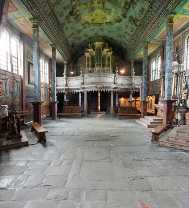 Zdjęcie nr 12: Kościół drewniany o konstrukcji zrębowej, elewacje jednolite, szalowane gontem. Wieża oraz kruchty zachodnia i południowa o konstrukcji słupowo-ramowej, kruchty szalowane deskami. Więźba dachowa drewniana, krokwiowa. Budynek na kamiennym podmurowaniu. 
Kościół orientowany, jednonawowy, nawa na rzucie prostokąta, prezbiterium węższe, wydłużone, zakończone trójbocznie. Do północnej ściany prezbiterium przylega zakrystia o wschodniej ścianie skośnej, będącej przedłużeniem bocznej ściany apsydy. 
Przy zachodniej ścianie nawy wieża na planie zbliżonym do kwadratu o wtórnym podziale na sale wystawiennicze (w przyziemiu wieży muzeum). Przy nawie od południa i przy wieży od frontu kruchty na planie kwadratu. 
Pomiędzy nawą a prezbiterium otwór tęczowy. 
Wnętrze nawy i prezbiterium nakryte pozornym sklepieniem kolebkowym, z zaskrzynieniami w nawie, podpartymi filarami o żłobkowanych trzonach, na cokołach, po trzy z każdej strony. Skrajem zaskrzynień nawy oraz górą ścian prezbiterium biegnie dekoracyjny gzyms drewniany, podparty w węgłach apsydy prezbiterialnej żłobkowanymi pilastrami. Łuk tęczowy półkolisty, wsparty na drewnianych konsolach. Otwory drzwiowe o prostokątnym wykroju zamknięte drzwiami obitymi deskami z metalowymi okuciami z prezbiterium do zakrystii, z nawy do kruchty południowej i z nawy do wieży. Okna w formie stojącego prostokąta zamkniętego łukiem odcinkowym, dwa w południowej ścianie prezbiterium, a w północnej dwa ślepe oraz cztery pary okien w północnej i południowej ścianie nawy. Na zamknięciu prezbiterium okulus z witrażem. Parapet chóru muzycznego w zachodniej części nawy, wsparty na dwóch drewnianych filarach, z wejściem z nawy po drabiniastych schodach z balustradą. Ściany i sklepienia pokryte polichromią z iluzjonistyczną architekturą i scenami figuralnymi. Posadzka kamienna.
Elewacja frontowa jednoosiowa. Na osi wejście do kruchty zachodniej. Korpus wieży o pochyłych ścianach, silnie zwężających się ku górze, zwieńczonych izbicą, ozdobioną u dołu koronką w formie zębów z frędzlami. Ściany kościoła, oprócz zakrystii i krucht szalowanych deskami, osłonięte rzędami gontów i opatrzone u dołu fartuchami. Na elewacji wschodniej ogrójec. 
Dach wyniosły, wspólny dla nawy i prezbiterium, hełm wieży cebulasty z latarnią, a w połowie długości dachu, nad nawą, wbudowana wieżyczka na sygnaturkę, wszystko kryte gontem. Kruchty nakryte osobnymi daszkami hełmowymi, baniastymi, krytymi gontem. 

Wokół kościoła rośnie starodrzew. Plac zamknięty kamiennym murem nakrytym drewnianym daszkiem dwuspadowym z 2 bramami i z 14 wieżyczkami (kapliczki-stacyjki) nakrytymi daszkami drewnianymi czterospadowymi. 