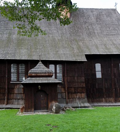 Zdjęcie nr 2: Kościół drewniany o konstrukcji zrębowej, elewacje jednolite, szalowane gontem. Wieża oraz kruchty zachodnia i południowa o konstrukcji słupowo-ramowej, kruchty szalowane deskami. Więźba dachowa drewniana, krokwiowa. Budynek na kamiennym podmurowaniu. 
Kościół orientowany, jednonawowy, nawa na rzucie prostokąta, prezbiterium węższe, wydłużone, zakończone trójbocznie. Do północnej ściany prezbiterium przylega zakrystia o wschodniej ścianie skośnej, będącej przedłużeniem bocznej ściany apsydy. 
Przy zachodniej ścianie nawy wieża na planie zbliżonym do kwadratu o wtórnym podziale na sale wystawiennicze (w przyziemiu wieży muzeum). Przy nawie od południa i przy wieży od frontu kruchty na planie kwadratu. 
Pomiędzy nawą a prezbiterium otwór tęczowy. 
Wnętrze nawy i prezbiterium nakryte pozornym sklepieniem kolebkowym, z zaskrzynieniami w nawie, podpartymi filarami o żłobkowanych trzonach, na cokołach, po trzy z każdej strony. Skrajem zaskrzynień nawy oraz górą ścian prezbiterium biegnie dekoracyjny gzyms drewniany, podparty w węgłach apsydy prezbiterialnej żłobkowanymi pilastrami. Łuk tęczowy półkolisty, wsparty na drewnianych konsolach. Otwory drzwiowe o prostokątnym wykroju zamknięte drzwiami obitymi deskami z metalowymi okuciami z prezbiterium do zakrystii, z nawy do kruchty południowej i z nawy do wieży. Okna w formie stojącego prostokąta zamkniętego łukiem odcinkowym, dwa w południowej ścianie prezbiterium, a w północnej dwa ślepe oraz cztery pary okien w północnej i południowej ścianie nawy. Na zamknięciu prezbiterium okulus z witrażem. Parapet chóru muzycznego w zachodniej części nawy, wsparty na dwóch drewnianych filarach, z wejściem z nawy po drabiniastych schodach z balustradą. Ściany i sklepienia pokryte polichromią z iluzjonistyczną architekturą i scenami figuralnymi. Posadzka kamienna.
Elewacja frontowa jednoosiowa. Na osi wejście do kruchty zachodniej. Korpus wieży o pochyłych ścianach, silnie zwężających się ku górze, zwieńczonych izbicą, ozdobioną u dołu koronką w formie zębów z frędzlami. Ściany kościoła, oprócz zakrystii i krucht szalowanych deskami, osłonięte rzędami gontów i opatrzone u dołu fartuchami. Na elewacji wschodniej ogrójec. 
Dach wyniosły, wspólny dla nawy i prezbiterium, hełm wieży cebulasty z latarnią, a w połowie długości dachu, nad nawą, wbudowana wieżyczka na sygnaturkę, wszystko kryte gontem. Kruchty nakryte osobnymi daszkami hełmowymi, baniastymi, krytymi gontem. 

Wokół kościoła rośnie starodrzew. Plac zamknięty kamiennym murem nakrytym drewnianym daszkiem dwuspadowym z 2 bramami i z 14 wieżyczkami (kapliczki-stacyjki) nakrytymi daszkami drewnianymi czterospadowymi. 