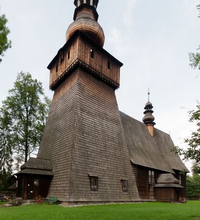 Zdjęcie nr 1: Kościół drewniany o konstrukcji zrębowej, elewacje jednolite, szalowane gontem. Wieża oraz kruchty zachodnia i południowa o konstrukcji słupowo-ramowej, kruchty szalowane deskami. Więźba dachowa drewniana, krokwiowa. Budynek na kamiennym podmurowaniu. 
Kościół orientowany, jednonawowy, nawa na rzucie prostokąta, prezbiterium węższe, wydłużone, zakończone trójbocznie. Do północnej ściany prezbiterium przylega zakrystia o wschodniej ścianie skośnej, będącej przedłużeniem bocznej ściany apsydy. 
Przy zachodniej ścianie nawy wieża na planie zbliżonym do kwadratu o wtórnym podziale na sale wystawiennicze (w przyziemiu wieży muzeum). Przy nawie od południa i przy wieży od frontu kruchty na planie kwadratu. 
Pomiędzy nawą a prezbiterium otwór tęczowy. 
Wnętrze nawy i prezbiterium nakryte pozornym sklepieniem kolebkowym, z zaskrzynieniami w nawie, podpartymi filarami o żłobkowanych trzonach, na cokołach, po trzy z każdej strony. Skrajem zaskrzynień nawy oraz górą ścian prezbiterium biegnie dekoracyjny gzyms drewniany, podparty w węgłach apsydy prezbiterialnej żłobkowanymi pilastrami. Łuk tęczowy półkolisty, wsparty na drewnianych konsolach. Otwory drzwiowe o prostokątnym wykroju zamknięte drzwiami obitymi deskami z metalowymi okuciami z prezbiterium do zakrystii, z nawy do kruchty południowej i z nawy do wieży. Okna w formie stojącego prostokąta zamkniętego łukiem odcinkowym, dwa w południowej ścianie prezbiterium, a w północnej dwa ślepe oraz cztery pary okien w północnej i południowej ścianie nawy. Na zamknięciu prezbiterium okulus z witrażem. Parapet chóru muzycznego w zachodniej części nawy, wsparty na dwóch drewnianych filarach, z wejściem z nawy po drabiniastych schodach z balustradą. Ściany i sklepienia pokryte polichromią z iluzjonistyczną architekturą i scenami figuralnymi. Posadzka kamienna.
Elewacja frontowa jednoosiowa. Na osi wejście do kruchty zachodniej. Korpus wieży o pochyłych ścianach, silnie zwężających się ku górze, zwieńczonych izbicą, ozdobioną u dołu koronką w formie zębów z frędzlami. Ściany kościoła, oprócz zakrystii i krucht szalowanych deskami, osłonięte rzędami gontów i opatrzone u dołu fartuchami. Na elewacji wschodniej ogrójec. 
Dach wyniosły, wspólny dla nawy i prezbiterium, hełm wieży cebulasty z latarnią, a w połowie długości dachu, nad nawą, wbudowana wieżyczka na sygnaturkę, wszystko kryte gontem. Kruchty nakryte osobnymi daszkami hełmowymi, baniastymi, krytymi gontem. 

Wokół kościoła rośnie starodrzew. Plac zamknięty kamiennym murem nakrytym drewnianym daszkiem dwuspadowym z 2 bramami i z 14 wieżyczkami (kapliczki-stacyjki) nakrytymi daszkami drewnianymi czterospadowymi. 