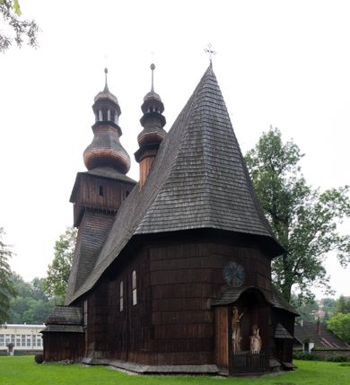 Zdjęcie nr 8: Kościół drewniany o konstrukcji zrębowej, elewacje jednolite, szalowane gontem. Wieża oraz kruchty zachodnia i południowa o konstrukcji słupowo-ramowej, kruchty szalowane deskami. Więźba dachowa drewniana, krokwiowa. Budynek na kamiennym podmurowaniu. 
Kościół orientowany, jednonawowy, nawa na rzucie prostokąta, prezbiterium węższe, wydłużone, zakończone trójbocznie. Do północnej ściany prezbiterium przylega zakrystia o wschodniej ścianie skośnej, będącej przedłużeniem bocznej ściany apsydy. 
Przy zachodniej ścianie nawy wieża na planie zbliżonym do kwadratu o wtórnym podziale na sale wystawiennicze (w przyziemiu wieży muzeum). Przy nawie od południa i przy wieży od frontu kruchty na planie kwadratu. 
Pomiędzy nawą a prezbiterium otwór tęczowy. 
Wnętrze nawy i prezbiterium nakryte pozornym sklepieniem kolebkowym, z zaskrzynieniami w nawie, podpartymi filarami o żłobkowanych trzonach, na cokołach, po trzy z każdej strony. Skrajem zaskrzynień nawy oraz górą ścian prezbiterium biegnie dekoracyjny gzyms drewniany, podparty w węgłach apsydy prezbiterialnej żłobkowanymi pilastrami. Łuk tęczowy półkolisty, wsparty na drewnianych konsolach. Otwory drzwiowe o prostokątnym wykroju zamknięte drzwiami obitymi deskami z metalowymi okuciami z prezbiterium do zakrystii, z nawy do kruchty południowej i z nawy do wieży. Okna w formie stojącego prostokąta zamkniętego łukiem odcinkowym, dwa w południowej ścianie prezbiterium, a w północnej dwa ślepe oraz cztery pary okien w północnej i południowej ścianie nawy. Na zamknięciu prezbiterium okulus z witrażem. Parapet chóru muzycznego w zachodniej części nawy, wsparty na dwóch drewnianych filarach, z wejściem z nawy po drabiniastych schodach z balustradą. Ściany i sklepienia pokryte polichromią z iluzjonistyczną architekturą i scenami figuralnymi. Posadzka kamienna.
Elewacja frontowa jednoosiowa. Na osi wejście do kruchty zachodniej. Korpus wieży o pochyłych ścianach, silnie zwężających się ku górze, zwieńczonych izbicą, ozdobioną u dołu koronką w formie zębów z frędzlami. Ściany kościoła, oprócz zakrystii i krucht szalowanych deskami, osłonięte rzędami gontów i opatrzone u dołu fartuchami. Na elewacji wschodniej ogrójec. 
Dach wyniosły, wspólny dla nawy i prezbiterium, hełm wieży cebulasty z latarnią, a w połowie długości dachu, nad nawą, wbudowana wieżyczka na sygnaturkę, wszystko kryte gontem. Kruchty nakryte osobnymi daszkami hełmowymi, baniastymi, krytymi gontem. 

Wokół kościoła rośnie starodrzew. Plac zamknięty kamiennym murem nakrytym drewnianym daszkiem dwuspadowym z 2 bramami i z 14 wieżyczkami (kapliczki-stacyjki) nakrytymi daszkami drewnianymi czterospadowymi. 