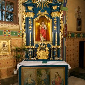 Zdjęcie nr 1: Ołtarz prostopadłościenny, z drewnianą mensą. W polu antepedium trzy przedstawienia: Najświętszego Serca Marii, Świętej Rodziny oraz Najświętszego Serca Jezusa, każde ujęte złoconą ramą. 
Nastawa ołtarzowa jednoosiowa, jednokondygnacyjna ze zwieńczeniem, ustawiona na cokole. Kondygnacja nastawy ujęta zdwojonymi pilastrami o kapitelach kompozytowych i kanelowanych trzonach, ustawionych pod kątem do środka. Ustawione na wyodrębnionych cokołach podpory dźwigają imposty oraz fragmenty przerwanego przyczółka. W polu środkowym nisza w formie stojącego prostokąta zamkniętego łukiem półkolistym nadwieszonym z uskokiem, ujęta profilowaną ramą. Zwieńczenie w formie zbliżonej do rombu, ujętego spływami wolutowymi, zamkniętego stykającymi się wolutami. W polu rzeźbione przedstawienie monogramu IHS na obłokach, ujęte glorią promienistą. Cokoły pilastrów dekorowane płycinami utworzonymi z ornamentu roślinnego. W partii trzonów zwisy kwiatowe, a impostów palmety. Rama pola środkowego ujęta od gry i dołu ornamentem roślinnym. Nastawa flankowana uszami utworzonymi z rocaille'u i ornamentu roślinnego. Struktura w kolorze granatowym; ornamentyka oraz profile złocone, obłoki srebrzone.
