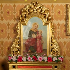 Zdjęcie nr 1: Feretron z obrazem Święta Anna nauczająca Marię. Podstawa w kształcie leżącego prostopadłościanu wspartego na kulistych nóżkach, profilowana, z w otworami na drążki, złocona, z czerwoną płyciną pośrodku. Obraz otoczony złoconą, profilowaną ramą w formie stojącego prostokąta zamkniętego od góry łukiem półkolistym nadwieszonym. Rama flankowana liśćmi akantu tworzącymi spływy wolutowe, ze zwieńczeniem utworzonym z liści akantu zwijanych w symetryczne esownice. Na uskokach ramy niewielkie wazony.
W polu obraz przedstawiający Annę z Marią. W centrum kompozycji Anna siedząca na ławie, zwrócona w trzech czwartych w lewo, z głową i rękoma skierowanymi w prawo, w stronę Marii, prawą ręką przytrzymuje otwartą księgę, opartą na kolanie, a lewą obejmuje córkę. Twarz ma podłużną, o dużych oczach, uniesionych brwiach, prostym nosie i małych ustach. Na głowie ma jasnożółty welon, jest ubrana w długą, ciemnozieloną suknię i czerwony płaszcz okrywający jej nogi. Spod szat wystaje jej prawa stopa w sandale, wsparta na stopniu. Maria stoi przy lewym boku matki, ukazana jest z profilu, z głową skierowaną w górę i dłońmi złożonymi w geście modlitwy. Ma pociągłą twarz o delikatnych rysach; okoloną długimi, jasnymi i falowanymi włosami. Jest ubrana w długą, różową suknię, przewiązaną w pasie wstążką, której końce skręcają się i rozwiewają do boku. Obie postacie mają wokół głów świetliste nimby.Tło sceny jednolite, jasnoniebieskie, w dolnej partii obrazu widoczna jasnobrązowa posadzka.