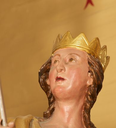 Zdjęcie nr 5: Figura ustawiona na niskiej, prostokątnej podstawie. Ukazana frontalnie, w wykroku lewej nogi, w lekkim odchyleniu ciała, z uniesioną głową skierowaną w lewo. Obie ręce ma wyciągnięte przed siebie, w prawej trzyma włócznię. Twarz ma szeroką, z niskim czołem i podkreślonym podbródkiem, o małych, migdałowatych oczach, niewielkim nosie i ustach. Włosy rzeźbione w lekko falowane pasma, ściśle przylegają do głowy i opadają na kark. Postać ma na głowie koronę otwartą. Ubrana jest w srebrzoną tunikę, sięgającą kolan, z podwiniętymi rękawami, złoconą zbroję tortową z piórami na ramionach, przewiązaną szarfą oraz złocony płaszcz z brązową podszewką, zarzucony na prawe ramię i opadający na lewą nogę. Na nogach ma srebrzone, wysokie buty. Polichromia ciała naturalistyczna.
