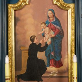 Zdjęcie nr 1: Obraz z przedstawieniem św. Stanisława Kostki z Matką Boską i Dzieciątkiem ujęty szeroką, złoconą ramą zamkniętą od góry łukiem nadwieszonym z uskokiem. Kompozycja skośna, po prawej stronie na obłokach stoi Matka Boska zwrócona delikatnie w prawo, która trzyma przed świętym na wyciągniętych rękach Dzieciątko Jezus. Maria ma owalną twarz, wysokie czoło, przymknięte oczy, wąski nos i małe usta;  jej głowę otacza wieniec z 12 gwiazd. Jest ubrana w czerwoną suknię i niebieski płaszcz z liliową podszewką, który niemal całkiem zakrywa jej jasne włosy. Płaszcz jest spięty na piersi i zarzucony na ramiona oraz nogi Marii. Trzymane przez nią Dzieciątko jest przepasane białą tkaniną, a obie ręce wyciąga w stronę świętego. Ma okrągłą twarz, krótkie jasne włosy, małe oczy, prosty nos i niewielkie usta; jego głowę otaczają złote promienie. Przed nimi na lewym kolanie klęczy św. Stanisław Kostka ukazany w trzech czwartych od tyłu, zwrócony w prawo. Obie ręce wyciąga w stronę Dzieciątka. Ma młodzieńczą twarz, krótkie, ciemne włosy. Ubrany jest w czarny strój zakonny, na nogach ma czarne buty. Przed nim, na stopniu gałązka lilii leży na otwartej księdze, za nim widoczny jest fragment pulpitu. Scena ukazana we wnętrzu, wypełnionym jasnofioletowymi i fioletowo-żółtymi obłokami; widoczny u dołu obrazu fragment podłogi w kolorze jasnobrązowym.