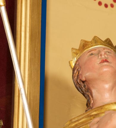 Zdjęcie nr 4: Figura ustawiona na niskiej, prostokątnej podstawie. Ukazana frontalnie, w silnym odchyleniu ciała, z uniesioną głową skierowaną w prawo. Lewą rękę kładzie na piersi, w prawej, wyciągniętej do przodu trzyma włócznię. Lewa noga ugięta, oparta na stopniu. Twarz ma szeroką, z niskim czołem i podkreślonym podbródkiem, o małych, migdałowatych oczach, niewielkim nosie i ustach. Włosy rzeźbione w lekko falowane pasma, ściśle przylegają do głowy i opadają na kark. Postać ma na głowie koronę otwartą. Ubrana jest w srebrzoną tunikę, sięgającą kolan, z podwiniętymi rękawami, złocony napierśnik przewiązany szarfą oraz złocony płaszcz z brązową podszewką, zarzucony pod szyją i opadający na plecy. Na nogach ma srebrzone, wysokie buty. Polichromią ciała naturalistyczna. 



