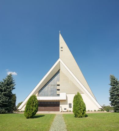 Zdjęcie nr 13: Budynek złożony z dwóch stopionych ze sobą brył, niższej o dwuspadowym dachu nakrywającym wnętrze prezbiterium i nawy oraz ostrosłupa wieży wpisanego w fasadę. Od strony prezbiterium dostawiona nieregularna bryła, niższa od kościoła, nakryta dwuspadowym dachem, mieszcząca zakrystię i kaplice Matki Boskiej. Połać dwustadowego dachu o nieregularnym, zygzakowatym konturze krawędzi, odsłaniającej przeszklone ściany, a miejscami sięgająca ziemi. Trójkątna w przekroju fasada z wieżą wpisaną w jej prawą połowę; lewa zaś w górnej połowie wypełniona witrażem, zamkniętym u dołu balkonem, nakrywającym przedsionek z wejściem do świątyni. Zewnętrzne elewacje kościoła pokryte są okładziną z wapienia pińczowskiego

Trójkątne w przekroju wnętrze podzielone na trzy nawy filarami. Prezbiterium zamknięte ścianą z wydzielonym trójkątem ołtarza głównego, złożonego z dwóch ścian pokrytych okładziną ceramiczną ustawionych pod kątem rozwartym, z otworem u szczytu na okno. Po przeciwnej stronie wnętrza wejście na wieżę i parapet chóru muzycznego. Na zakończeniu lewej nawy wejście do kaplicy Matki Boskiej, na zakończeniu prawej nawy zaaranżowana kaplica bł. Anieli Salawy. Ściany boczne całkowicie przeszklone; połowę przestrzeni fasady wypełnia witraż o polu w formie trójkąta o kącie prostym. W kaplicy Matki Boskiej otwory w formie szczelin oświetlające wnętrze umieszczone nieregularnie w polu ściany. 




