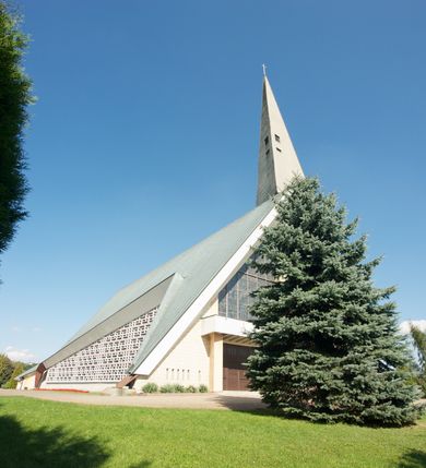 Zdjęcie nr 3: Budynek złożony z dwóch stopionych ze sobą brył, niższej o dwuspadowym dachu nakrywającym wnętrze prezbiterium i nawy oraz ostrosłupa wieży wpisanego w fasadę. Od strony prezbiterium dostawiona nieregularna bryła, niższa od kościoła, nakryta dwuspadowym dachem, mieszcząca zakrystię i kaplice Matki Boskiej. Połać dwustadowego dachu o nieregularnym, zygzakowatym konturze krawędzi, odsłaniającej przeszklone ściany, a miejscami sięgająca ziemi. Trójkątna w przekroju fasada z wieżą wpisaną w jej prawą połowę; lewa zaś w górnej połowie wypełniona witrażem, zamkniętym u dołu balkonem, nakrywającym przedsionek z wejściem do świątyni. Zewnętrzne elewacje kościoła pokryte są okładziną z wapienia pińczowskiego

Trójkątne w przekroju wnętrze podzielone na trzy nawy filarami. Prezbiterium zamknięte ścianą z wydzielonym trójkątem ołtarza głównego, złożonego z dwóch ścian pokrytych okładziną ceramiczną ustawionych pod kątem rozwartym, z otworem u szczytu na okno. Po przeciwnej stronie wnętrza wejście na wieżę i parapet chóru muzycznego. Na zakończeniu lewej nawy wejście do kaplicy Matki Boskiej, na zakończeniu prawej nawy zaaranżowana kaplica bł. Anieli Salawy. Ściany boczne całkowicie przeszklone; połowę przestrzeni fasady wypełnia witraż o polu w formie trójkąta o kącie prostym. W kaplicy Matki Boskiej otwory w formie szczelin oświetlające wnętrze umieszczone nieregularnie w polu ściany. 




