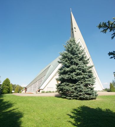 Zdjęcie nr 12: Budynek złożony z dwóch stopionych ze sobą brył, niższej o dwuspadowym dachu nakrywającym wnętrze prezbiterium i nawy oraz ostrosłupa wieży wpisanego w fasadę. Od strony prezbiterium dostawiona nieregularna bryła, niższa od kościoła, nakryta dwuspadowym dachem, mieszcząca zakrystię i kaplice Matki Boskiej. Połać dwustadowego dachu o nieregularnym, zygzakowatym konturze krawędzi, odsłaniającej przeszklone ściany, a miejscami sięgająca ziemi. Trójkątna w przekroju fasada z wieżą wpisaną w jej prawą połowę; lewa zaś w górnej połowie wypełniona witrażem, zamkniętym u dołu balkonem, nakrywającym przedsionek z wejściem do świątyni. Zewnętrzne elewacje kościoła pokryte są okładziną z wapienia pińczowskiego

Trójkątne w przekroju wnętrze podzielone na trzy nawy filarami. Prezbiterium zamknięte ścianą z wydzielonym trójkątem ołtarza głównego, złożonego z dwóch ścian pokrytych okładziną ceramiczną ustawionych pod kątem rozwartym, z otworem u szczytu na okno. Po przeciwnej stronie wnętrza wejście na wieżę i parapet chóru muzycznego. Na zakończeniu lewej nawy wejście do kaplicy Matki Boskiej, na zakończeniu prawej nawy zaaranżowana kaplica bł. Anieli Salawy. Ściany boczne całkowicie przeszklone; połowę przestrzeni fasady wypełnia witraż o polu w formie trójkąta o kącie prostym. W kaplicy Matki Boskiej otwory w formie szczelin oświetlające wnętrze umieszczone nieregularnie w polu ściany. 




