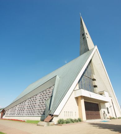 Zdjęcie nr 4: Budynek złożony z dwóch stopionych ze sobą brył, niższej o dwuspadowym dachu nakrywającym wnętrze prezbiterium i nawy oraz ostrosłupa wieży wpisanego w fasadę. Od strony prezbiterium dostawiona nieregularna bryła, niższa od kościoła, nakryta dwuspadowym dachem, mieszcząca zakrystię i kaplice Matki Boskiej. Połać dwustadowego dachu o nieregularnym, zygzakowatym konturze krawędzi, odsłaniającej przeszklone ściany, a miejscami sięgająca ziemi. Trójkątna w przekroju fasada z wieżą wpisaną w jej prawą połowę; lewa zaś w górnej połowie wypełniona witrażem, zamkniętym u dołu balkonem, nakrywającym przedsionek z wejściem do świątyni. Zewnętrzne elewacje kościoła pokryte są okładziną z wapienia pińczowskiego

Trójkątne w przekroju wnętrze podzielone na trzy nawy filarami. Prezbiterium zamknięte ścianą z wydzielonym trójkątem ołtarza głównego, złożonego z dwóch ścian pokrytych okładziną ceramiczną ustawionych pod kątem rozwartym, z otworem u szczytu na okno. Po przeciwnej stronie wnętrza wejście na wieżę i parapet chóru muzycznego. Na zakończeniu lewej nawy wejście do kaplicy Matki Boskiej, na zakończeniu prawej nawy zaaranżowana kaplica bł. Anieli Salawy. Ściany boczne całkowicie przeszklone; połowę przestrzeni fasady wypełnia witraż o polu w formie trójkąta o kącie prostym. W kaplicy Matki Boskiej otwory w formie szczelin oświetlające wnętrze umieszczone nieregularnie w polu ściany. 




