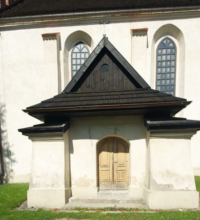 Zdjęcie nr 6: Kościół murowany z kamienia, z użyciem cegły, tynkowany; orientowany, jednonawowy. Prezbiterium węższe od nawy, zwężające się, na rzucie zbliżonym do trapezu. Przy północnej ścianie zakrystia w rzucie zbliżonym do kwadratu, z ukośną ścianą południową. Nawa na planie prostokąta, z przylegającymi od południa kruchtą i wieżą od zachodu na rzucie prostokąta. Nawa i zakrystia opięte szkarpami. 
Wnętrze nakryte stropami drewnianymi. Wątki ceglane i murowane ścian odsłonięte. Zamiast posadzki wylewka betonowa (posadzki kamienne zdemontowane). Otwór tęczowy półkolisty. Otwory okienne nawy i prezbiterium w liczbie czterech na południowej ścianie i jednego na północnej w części prezbiterium; w formie wydłużonego stojącego prostokąta zamkniętego półkoliście ze ściętymi glifami, bez obramień. Na ścianie zamykającej prezbiterium niewielki okulus. Na ścianie zachodniej niewielkie otwory okienne w formie stojącego prostokąta, dwa zamknięte ostrołukowo (przesłonięte), jeden zamknięty łukiem odcinkowym oraz dwa okulusy (zamurowane). Otwory okienne wieży ostrołukowe, z profilowanymi obramieniami kamiennymi. W zakrystii małe kwadratowe okienko przesłonięte kratownicą. Otwory drzwiowe: w wejściu do przyziemia wieży od zachodu, otwór w formie stojącego prostokąta zamkniętego łukiem ostrym, w kamiennym obramieniu zwieńczony kamienną tablicą (z datą budowy wieży „1868”), z drewnianymi drzwiami płycinowymi, dwuskrzydłowymi; w przejściu z przyziemia wieży do nawy otwór w formie stojącego prostokąta zamkniętego półkoliście (pierwotnie zamkniętego łukiem odcinkowym), przesłonięty metalową kratą; w wejściu do kruchty południowej otwór w formie stojącego prostokąta zamknięty łukiem odcinkowym, z drzwiami płycinowymi, dwuskrzydłowymi; w przejściu z kruchty do nawy otwór w formie stojącego prostokąta zamknięty półkoliście z drewnianymi drzwiami z okuciami, zamkiem i antabą; w wejściu do zakrystii od zewnętrz otwór prostokątny, z drzwiami jednoskrzydłowymi, płycinowymi; w przejściu z zakrystii do nawy otwór w formie stojącego prostokąta, w kamiennym obramieniu, z drzwiami z okuciami i zamkiem. Elewacje tynkowane, zamknięte profilowanymi gzymsami podokapowymi. Nawa, zakrystia i kruchta opięte szkarpami (przy nawie uskokowymi z daszkami okapowymi). Fasada zamknięta ceglanym szczytem, dekorowanym schodkowym krenelażem, z dwoma niewielkimi, smukłymi otworami okiennymi zamkniętymi ostrołukowo. 
Wieża trójkondygnacyjna, bez podziałów architektonicznych, druga kondygnacja zamknięta daszkiem okapowym. Zwieńczona dachem namiotowym z latarnią na planie ośmioboku, zamkniętą dachem wieżowym, pobitym blachą.
Pierwotne dachy siodłowe, o odrębnych kalenicach dla nawy i prezbiterium, kryte gontem; więźba drewniana, konstrukcji krokwiowej. Nad nawą wieżyczka na sygnaturkę z hełmem baniastym z latarnią, kryta blachą. Kruchtę przykrywa dach dwuspadowy, kryty gontem. 
