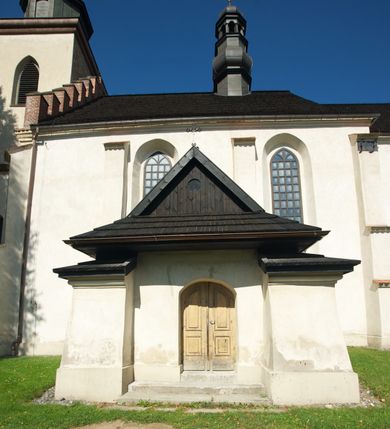 Zdjęcie nr 17: Kościół murowany z kamienia, z użyciem cegły, tynkowany; orientowany, jednonawowy. Prezbiterium węższe od nawy, zwężające się, na rzucie zbliżonym do trapezu. Przy północnej ścianie zakrystia w rzucie zbliżonym do kwadratu, z ukośną ścianą południową. Nawa na planie prostokąta, z przylegającymi od południa kruchtą i wieżą od zachodu na rzucie prostokąta. Nawa i zakrystia opięte szkarpami. 
Wnętrze nakryte stropami drewnianymi. Wątki ceglane i murowane ścian odsłonięte. Zamiast posadzki wylewka betonowa (posadzki kamienne zdemontowane). Otwór tęczowy półkolisty. Otwory okienne nawy i prezbiterium w liczbie czterech na południowej ścianie i jednego na północnej w części prezbiterium; w formie wydłużonego stojącego prostokąta zamkniętego półkoliście ze ściętymi glifami, bez obramień. Na ścianie zamykającej prezbiterium niewielki okulus. Na ścianie zachodniej niewielkie otwory okienne w formie stojącego prostokąta, dwa zamknięte ostrołukowo (przesłonięte), jeden zamknięty łukiem odcinkowym oraz dwa okulusy (zamurowane). Otwory okienne wieży ostrołukowe, z profilowanymi obramieniami kamiennymi. W zakrystii małe kwadratowe okienko przesłonięte kratownicą. Otwory drzwiowe: w wejściu do przyziemia wieży od zachodu, otwór w formie stojącego prostokąta zamkniętego łukiem ostrym, w kamiennym obramieniu zwieńczony kamienną tablicą (z datą budowy wieży „1868”), z drewnianymi drzwiami płycinowymi, dwuskrzydłowymi; w przejściu z przyziemia wieży do nawy otwór w formie stojącego prostokąta zamkniętego półkoliście (pierwotnie zamkniętego łukiem odcinkowym), przesłonięty metalową kratą; w wejściu do kruchty południowej otwór w formie stojącego prostokąta zamknięty łukiem odcinkowym, z drzwiami płycinowymi, dwuskrzydłowymi; w przejściu z kruchty do nawy otwór w formie stojącego prostokąta zamknięty półkoliście z drewnianymi drzwiami z okuciami, zamkiem i antabą; w wejściu do zakrystii od zewnętrz otwór prostokątny, z drzwiami jednoskrzydłowymi, płycinowymi; w przejściu z zakrystii do nawy otwór w formie stojącego prostokąta, w kamiennym obramieniu, z drzwiami z okuciami i zamkiem. Elewacje tynkowane, zamknięte profilowanymi gzymsami podokapowymi. Nawa, zakrystia i kruchta opięte szkarpami (przy nawie uskokowymi z daszkami okapowymi). Fasada zamknięta ceglanym szczytem, dekorowanym schodkowym krenelażem, z dwoma niewielkimi, smukłymi otworami okiennymi zamkniętymi ostrołukowo. 
Wieża trójkondygnacyjna, bez podziałów architektonicznych, druga kondygnacja zamknięta daszkiem okapowym. Zwieńczona dachem namiotowym z latarnią na planie ośmioboku, zamkniętą dachem wieżowym, pobitym blachą.
Pierwotne dachy siodłowe, o odrębnych kalenicach dla nawy i prezbiterium, kryte gontem; więźba drewniana, konstrukcji krokwiowej. Nad nawą wieżyczka na sygnaturkę z hełmem baniastym z latarnią, kryta blachą. Kruchtę przykrywa dach dwuspadowy, kryty gontem. 
