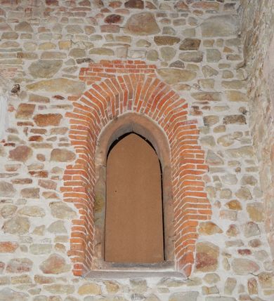 Zdjęcie nr 5: Kościół murowany z kamienia, z użyciem cegły, tynkowany; orientowany, jednonawowy. Prezbiterium węższe od nawy, zwężające się, na rzucie zbliżonym do trapezu. Przy północnej ścianie zakrystia w rzucie zbliżonym do kwadratu, z ukośną ścianą południową. Nawa na planie prostokąta, z przylegającymi od południa kruchtą i wieżą od zachodu na rzucie prostokąta. Nawa i zakrystia opięte szkarpami. 
Wnętrze nakryte stropami drewnianymi. Wątki ceglane i murowane ścian odsłonięte. Zamiast posadzki wylewka betonowa (posadzki kamienne zdemontowane). Otwór tęczowy półkolisty. Otwory okienne nawy i prezbiterium w liczbie czterech na południowej ścianie i jednego na północnej w części prezbiterium; w formie wydłużonego stojącego prostokąta zamkniętego półkoliście ze ściętymi glifami, bez obramień. Na ścianie zamykającej prezbiterium niewielki okulus. Na ścianie zachodniej niewielkie otwory okienne w formie stojącego prostokąta, dwa zamknięte ostrołukowo (przesłonięte), jeden zamknięty łukiem odcinkowym oraz dwa okulusy (zamurowane). Otwory okienne wieży ostrołukowe, z profilowanymi obramieniami kamiennymi. W zakrystii małe kwadratowe okienko przesłonięte kratownicą. Otwory drzwiowe: w wejściu do przyziemia wieży od zachodu, otwór w formie stojącego prostokąta zamkniętego łukiem ostrym, w kamiennym obramieniu zwieńczony kamienną tablicą (z datą budowy wieży „1868”), z drewnianymi drzwiami płycinowymi, dwuskrzydłowymi; w przejściu z przyziemia wieży do nawy otwór w formie stojącego prostokąta zamkniętego półkoliście (pierwotnie zamkniętego łukiem odcinkowym), przesłonięty metalową kratą; w wejściu do kruchty południowej otwór w formie stojącego prostokąta zamknięty łukiem odcinkowym, z drzwiami płycinowymi, dwuskrzydłowymi; w przejściu z kruchty do nawy otwór w formie stojącego prostokąta zamknięty półkoliście z drewnianymi drzwiami z okuciami, zamkiem i antabą; w wejściu do zakrystii od zewnętrz otwór prostokątny, z drzwiami jednoskrzydłowymi, płycinowymi; w przejściu z zakrystii do nawy otwór w formie stojącego prostokąta, w kamiennym obramieniu, z drzwiami z okuciami i zamkiem. Elewacje tynkowane, zamknięte profilowanymi gzymsami podokapowymi. Nawa, zakrystia i kruchta opięte szkarpami (przy nawie uskokowymi z daszkami okapowymi). Fasada zamknięta ceglanym szczytem, dekorowanym schodkowym krenelażem, z dwoma niewielkimi, smukłymi otworami okiennymi zamkniętymi ostrołukowo. 
Wieża trójkondygnacyjna, bez podziałów architektonicznych, druga kondygnacja zamknięta daszkiem okapowym. Zwieńczona dachem namiotowym z latarnią na planie ośmioboku, zamkniętą dachem wieżowym, pobitym blachą.
Pierwotne dachy siodłowe, o odrębnych kalenicach dla nawy i prezbiterium, kryte gontem; więźba drewniana, konstrukcji krokwiowej. Nad nawą wieżyczka na sygnaturkę z hełmem baniastym z latarnią, kryta blachą. Kruchtę przykrywa dach dwuspadowy, kryty gontem. 
