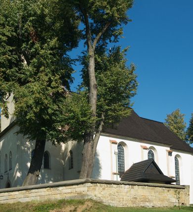 Zdjęcie nr 20: Kościół murowany z kamienia, z użyciem cegły, tynkowany; orientowany, jednonawowy. Prezbiterium węższe od nawy, zwężające się, na rzucie zbliżonym do trapezu. Przy północnej ścianie zakrystia w rzucie zbliżonym do kwadratu, z ukośną ścianą południową. Nawa na planie prostokąta, z przylegającymi od południa kruchtą i wieżą od zachodu na rzucie prostokąta. Nawa i zakrystia opięte szkarpami. 
Wnętrze nakryte stropami drewnianymi. Wątki ceglane i murowane ścian odsłonięte. Zamiast posadzki wylewka betonowa (posadzki kamienne zdemontowane). Otwór tęczowy półkolisty. Otwory okienne nawy i prezbiterium w liczbie czterech na południowej ścianie i jednego na północnej w części prezbiterium; w formie wydłużonego stojącego prostokąta zamkniętego półkoliście ze ściętymi glifami, bez obramień. Na ścianie zamykającej prezbiterium niewielki okulus. Na ścianie zachodniej niewielkie otwory okienne w formie stojącego prostokąta, dwa zamknięte ostrołukowo (przesłonięte), jeden zamknięty łukiem odcinkowym oraz dwa okulusy (zamurowane). Otwory okienne wieży ostrołukowe, z profilowanymi obramieniami kamiennymi. W zakrystii małe kwadratowe okienko przesłonięte kratownicą. Otwory drzwiowe: w wejściu do przyziemia wieży od zachodu, otwór w formie stojącego prostokąta zamkniętego łukiem ostrym, w kamiennym obramieniu zwieńczony kamienną tablicą (z datą budowy wieży „1868”), z drewnianymi drzwiami płycinowymi, dwuskrzydłowymi; w przejściu z przyziemia wieży do nawy otwór w formie stojącego prostokąta zamkniętego półkoliście (pierwotnie zamkniętego łukiem odcinkowym), przesłonięty metalową kratą; w wejściu do kruchty południowej otwór w formie stojącego prostokąta zamknięty łukiem odcinkowym, z drzwiami płycinowymi, dwuskrzydłowymi; w przejściu z kruchty do nawy otwór w formie stojącego prostokąta zamknięty półkoliście z drewnianymi drzwiami z okuciami, zamkiem i antabą; w wejściu do zakrystii od zewnętrz otwór prostokątny, z drzwiami jednoskrzydłowymi, płycinowymi; w przejściu z zakrystii do nawy otwór w formie stojącego prostokąta, w kamiennym obramieniu, z drzwiami z okuciami i zamkiem. Elewacje tynkowane, zamknięte profilowanymi gzymsami podokapowymi. Nawa, zakrystia i kruchta opięte szkarpami (przy nawie uskokowymi z daszkami okapowymi). Fasada zamknięta ceglanym szczytem, dekorowanym schodkowym krenelażem, z dwoma niewielkimi, smukłymi otworami okiennymi zamkniętymi ostrołukowo. 
Wieża trójkondygnacyjna, bez podziałów architektonicznych, druga kondygnacja zamknięta daszkiem okapowym. Zwieńczona dachem namiotowym z latarnią na planie ośmioboku, zamkniętą dachem wieżowym, pobitym blachą.
Pierwotne dachy siodłowe, o odrębnych kalenicach dla nawy i prezbiterium, kryte gontem; więźba drewniana, konstrukcji krokwiowej. Nad nawą wieżyczka na sygnaturkę z hełmem baniastym z latarnią, kryta blachą. Kruchtę przykrywa dach dwuspadowy, kryty gontem. 
