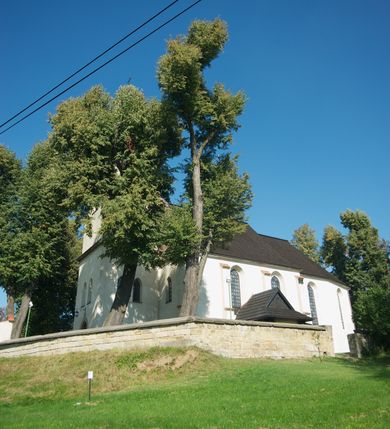 Zdjęcie nr 22: Kościół murowany z kamienia, z użyciem cegły, tynkowany; orientowany, jednonawowy. Prezbiterium węższe od nawy, zwężające się, na rzucie zbliżonym do trapezu. Przy północnej ścianie zakrystia w rzucie zbliżonym do kwadratu, z ukośną ścianą południową. Nawa na planie prostokąta, z przylegającymi od południa kruchtą i wieżą od zachodu na rzucie prostokąta. Nawa i zakrystia opięte szkarpami. 
Wnętrze nakryte stropami drewnianymi. Wątki ceglane i murowane ścian odsłonięte. Zamiast posadzki wylewka betonowa (posadzki kamienne zdemontowane). Otwór tęczowy półkolisty. Otwory okienne nawy i prezbiterium w liczbie czterech na południowej ścianie i jednego na północnej w części prezbiterium; w formie wydłużonego stojącego prostokąta zamkniętego półkoliście ze ściętymi glifami, bez obramień. Na ścianie zamykającej prezbiterium niewielki okulus. Na ścianie zachodniej niewielkie otwory okienne w formie stojącego prostokąta, dwa zamknięte ostrołukowo (przesłonięte), jeden zamknięty łukiem odcinkowym oraz dwa okulusy (zamurowane). Otwory okienne wieży ostrołukowe, z profilowanymi obramieniami kamiennymi. W zakrystii małe kwadratowe okienko przesłonięte kratownicą. Otwory drzwiowe: w wejściu do przyziemia wieży od zachodu, otwór w formie stojącego prostokąta zamkniętego łukiem ostrym, w kamiennym obramieniu zwieńczony kamienną tablicą (z datą budowy wieży „1868”), z drewnianymi drzwiami płycinowymi, dwuskrzydłowymi; w przejściu z przyziemia wieży do nawy otwór w formie stojącego prostokąta zamkniętego półkoliście (pierwotnie zamkniętego łukiem odcinkowym), przesłonięty metalową kratą; w wejściu do kruchty południowej otwór w formie stojącego prostokąta zamknięty łukiem odcinkowym, z drzwiami płycinowymi, dwuskrzydłowymi; w przejściu z kruchty do nawy otwór w formie stojącego prostokąta zamknięty półkoliście z drewnianymi drzwiami z okuciami, zamkiem i antabą; w wejściu do zakrystii od zewnętrz otwór prostokątny, z drzwiami jednoskrzydłowymi, płycinowymi; w przejściu z zakrystii do nawy otwór w formie stojącego prostokąta, w kamiennym obramieniu, z drzwiami z okuciami i zamkiem. Elewacje tynkowane, zamknięte profilowanymi gzymsami podokapowymi. Nawa, zakrystia i kruchta opięte szkarpami (przy nawie uskokowymi z daszkami okapowymi). Fasada zamknięta ceglanym szczytem, dekorowanym schodkowym krenelażem, z dwoma niewielkimi, smukłymi otworami okiennymi zamkniętymi ostrołukowo. 
Wieża trójkondygnacyjna, bez podziałów architektonicznych, druga kondygnacja zamknięta daszkiem okapowym. Zwieńczona dachem namiotowym z latarnią na planie ośmioboku, zamkniętą dachem wieżowym, pobitym blachą.
Pierwotne dachy siodłowe, o odrębnych kalenicach dla nawy i prezbiterium, kryte gontem; więźba drewniana, konstrukcji krokwiowej. Nad nawą wieżyczka na sygnaturkę z hełmem baniastym z latarnią, kryta blachą. Kruchtę przykrywa dach dwuspadowy, kryty gontem. 
