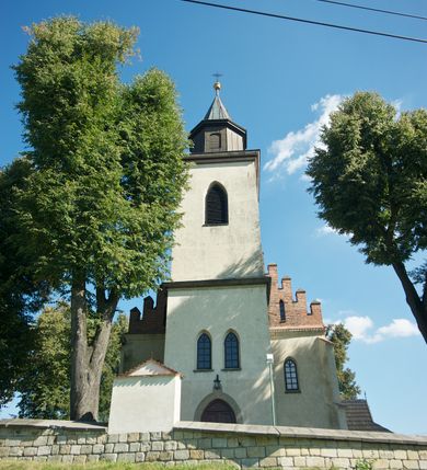 Zdjęcie nr 2: Kościół murowany z kamienia, z użyciem cegły, tynkowany; orientowany, jednonawowy. Prezbiterium węższe od nawy, zwężające się, na rzucie zbliżonym do trapezu. Przy północnej ścianie zakrystia w rzucie zbliżonym do kwadratu, z ukośną ścianą południową. Nawa na planie prostokąta, z przylegającymi od południa kruchtą i wieżą od zachodu na rzucie prostokąta. Nawa i zakrystia opięte szkarpami. 
Wnętrze nakryte stropami drewnianymi. Wątki ceglane i murowane ścian odsłonięte. Zamiast posadzki wylewka betonowa (posadzki kamienne zdemontowane). Otwór tęczowy półkolisty. Otwory okienne nawy i prezbiterium w liczbie czterech na południowej ścianie i jednego na północnej w części prezbiterium; w formie wydłużonego stojącego prostokąta zamkniętego półkoliście ze ściętymi glifami, bez obramień. Na ścianie zamykającej prezbiterium niewielki okulus. Na ścianie zachodniej niewielkie otwory okienne w formie stojącego prostokąta, dwa zamknięte ostrołukowo (przesłonięte), jeden zamknięty łukiem odcinkowym oraz dwa okulusy (zamurowane). Otwory okienne wieży ostrołukowe, z profilowanymi obramieniami kamiennymi. W zakrystii małe kwadratowe okienko przesłonięte kratownicą. Otwory drzwiowe: w wejściu do przyziemia wieży od zachodu, otwór w formie stojącego prostokąta zamkniętego łukiem ostrym, w kamiennym obramieniu zwieńczony kamienną tablicą (z datą budowy wieży „1868”), z drewnianymi drzwiami płycinowymi, dwuskrzydłowymi; w przejściu z przyziemia wieży do nawy otwór w formie stojącego prostokąta zamkniętego półkoliście (pierwotnie zamkniętego łukiem odcinkowym), przesłonięty metalową kratą; w wejściu do kruchty południowej otwór w formie stojącego prostokąta zamknięty łukiem odcinkowym, z drzwiami płycinowymi, dwuskrzydłowymi; w przejściu z kruchty do nawy otwór w formie stojącego prostokąta zamknięty półkoliście z drewnianymi drzwiami z okuciami, zamkiem i antabą; w wejściu do zakrystii od zewnętrz otwór prostokątny, z drzwiami jednoskrzydłowymi, płycinowymi; w przejściu z zakrystii do nawy otwór w formie stojącego prostokąta, w kamiennym obramieniu, z drzwiami z okuciami i zamkiem. Elewacje tynkowane, zamknięte profilowanymi gzymsami podokapowymi. Nawa, zakrystia i kruchta opięte szkarpami (przy nawie uskokowymi z daszkami okapowymi). Fasada zamknięta ceglanym szczytem, dekorowanym schodkowym krenelażem, z dwoma niewielkimi, smukłymi otworami okiennymi zamkniętymi ostrołukowo. 
Wieża trójkondygnacyjna, bez podziałów architektonicznych, druga kondygnacja zamknięta daszkiem okapowym. Zwieńczona dachem namiotowym z latarnią na planie ośmioboku, zamkniętą dachem wieżowym, pobitym blachą.
Pierwotne dachy siodłowe, o odrębnych kalenicach dla nawy i prezbiterium, kryte gontem; więźba drewniana, konstrukcji krokwiowej. Nad nawą wieżyczka na sygnaturkę z hełmem baniastym z latarnią, kryta blachą. Kruchtę przykrywa dach dwuspadowy, kryty gontem. 
