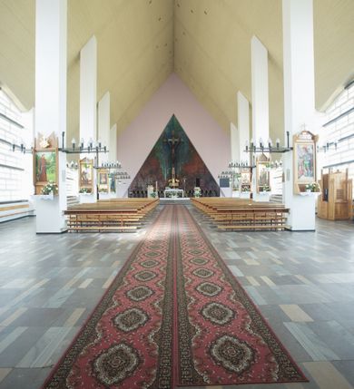 Zdjęcie nr 2: Okładzina ceramiczna pokrywa dwie ściany zamykające prezbiterium, łączące się pod kątem rozwartym i doświetlone pośrodku przez wpadające z górnego świetlika światło. Płyty są płaskorzeźbione i opracowane reliefowo, w kolorystyce błękitnej i seledynowej spływającej od szczytu ściany i przechodzącej w intensywną czerwień i brązy.