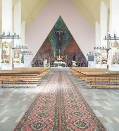 Zdjęcie nr 3: Okładzina ceramiczna pokrywa dwie ściany zamykające prezbiterium, łączące się pod kątem rozwartym i doświetlone pośrodku przez wpadające z górnego świetlika światło. Płyty są płaskorzeźbione i opracowane reliefowo, w kolorystyce błękitnej i seledynowej spływającej od szczytu ściany i przechodzącej w intensywną czerwień i brązy.