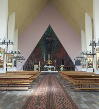 Zdjęcie nr 4: Okładzina ceramiczna pokrywa dwie ściany zamykające prezbiterium, łączące się pod kątem rozwartym i doświetlone pośrodku przez wpadające z górnego świetlika światło. Płyty są płaskorzeźbione i opracowane reliefowo, w kolorystyce błękitnej i seledynowej spływającej od szczytu ściany i przechodzącej w intensywną czerwień i brązy.