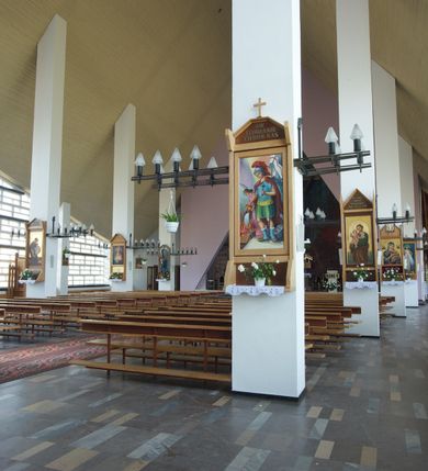 Zdjęcie nr 5: Okładzina ceramiczna pokrywa dwie ściany zamykające prezbiterium, łączące się pod kątem rozwartym i doświetlone pośrodku przez wpadające z górnego świetlika światło. Płyty są płaskorzeźbione i opracowane reliefowo, w kolorystyce błękitnej i seledynowej spływającej od szczytu ściany i przechodzącej w intensywną czerwień i brązy.