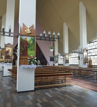 Zdjęcie nr 6: Okładzina ceramiczna pokrywa dwie ściany zamykające prezbiterium, łączące się pod kątem rozwartym i doświetlone pośrodku przez wpadające z górnego świetlika światło. Płyty są płaskorzeźbione i opracowane reliefowo, w kolorystyce błękitnej i seledynowej spływającej od szczytu ściany i przechodzącej w intensywną czerwień i brązy.
